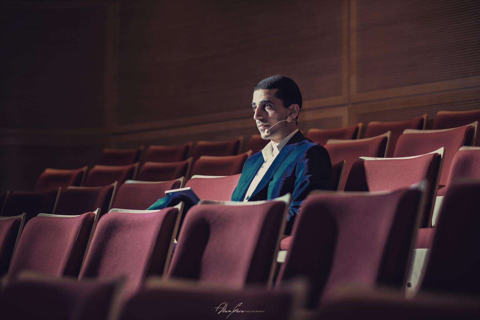 Hasan Abo Shally seated in an auditorium with a stage microphone before a talk